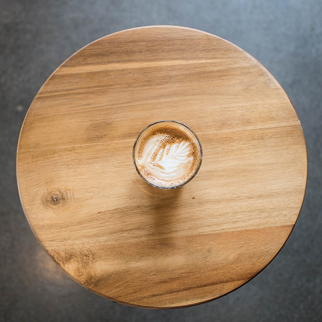 Latte in glass on circular wooden table