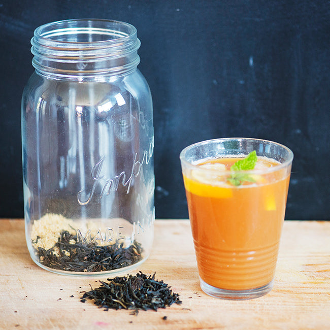 Mason jar with loose leaf black tea and cane sugar, glass with iced black tea on wooden counter