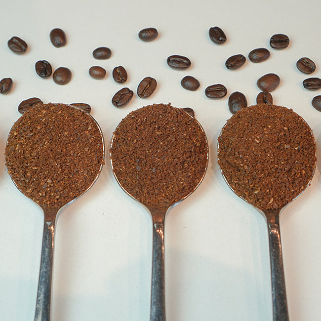 Three spoons with ground coffee, coffee beans placed beside