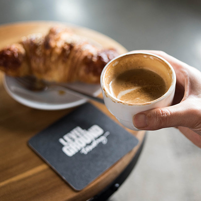 Hand holds espresso in white cup, croissant in background