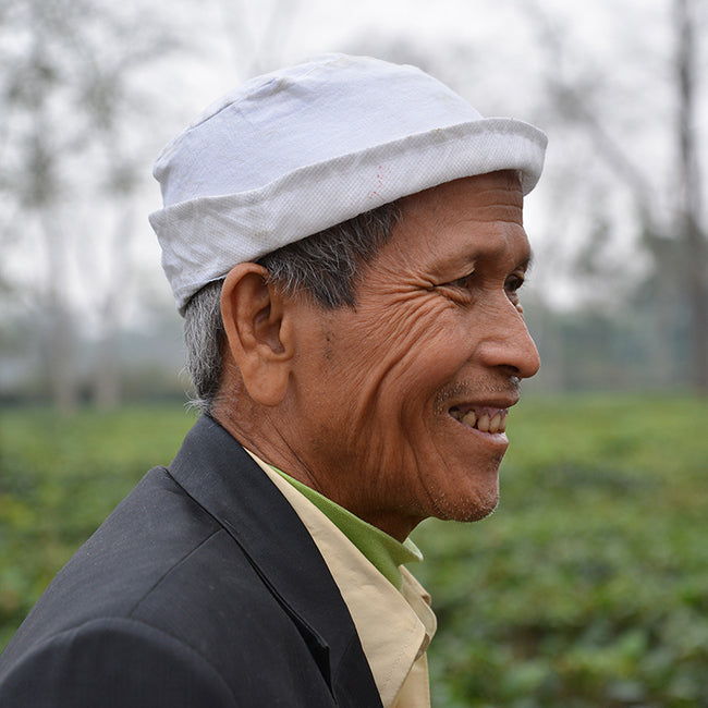 Side profile tea farmer wearing white cap in tea garden smiling