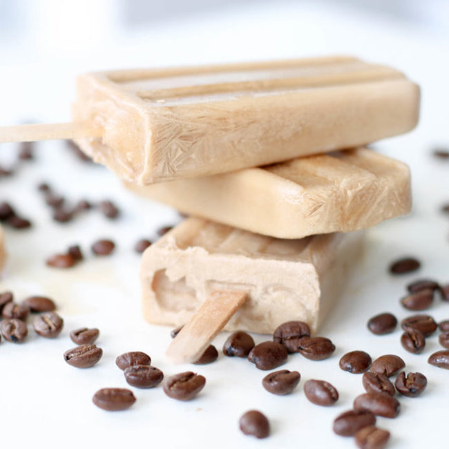 Three coconut cream coffee popsicles stacked, coffee beans scattered around