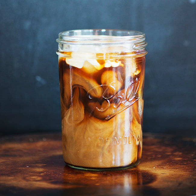 Mason jar on wooden counter with coffee and cream mixing