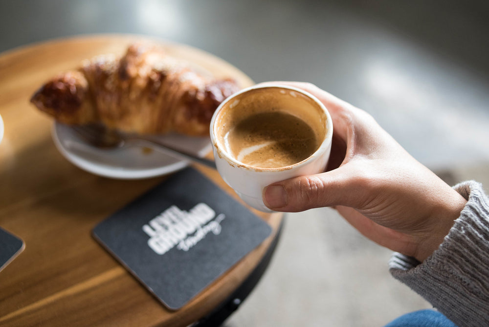 Hand holding a cup of coffee, a pastry in the background. 